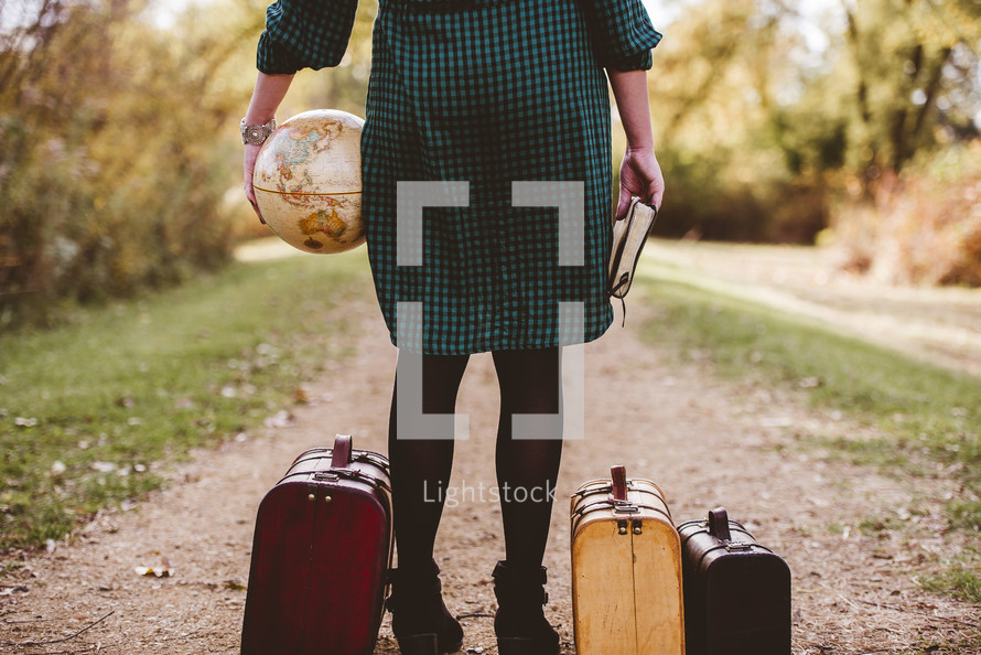a woman holding a globe and Bible standing next to luggage 