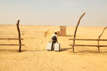 man pulling luggage through sand to a train station in a desert  