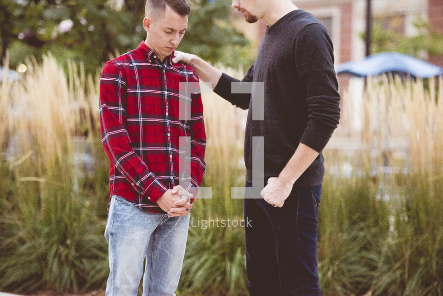 two men praying together outdoors 