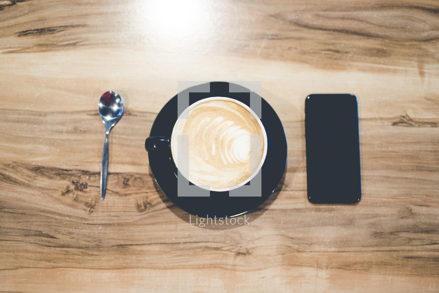latte, cellphone, and spoon on a wood table 