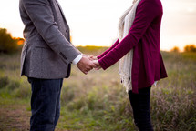 couple standing outdoors in a field holding hands 