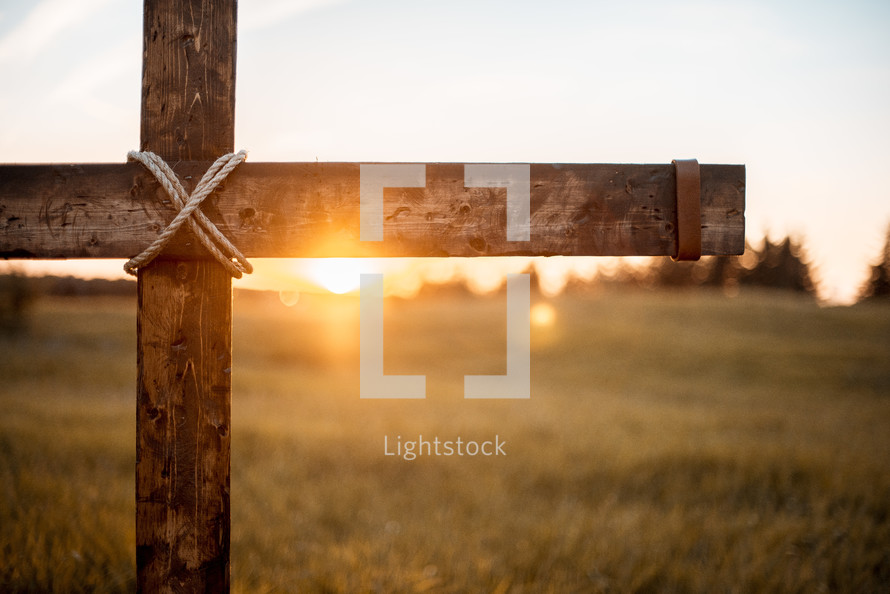 wooden cross in a field at sunset 
