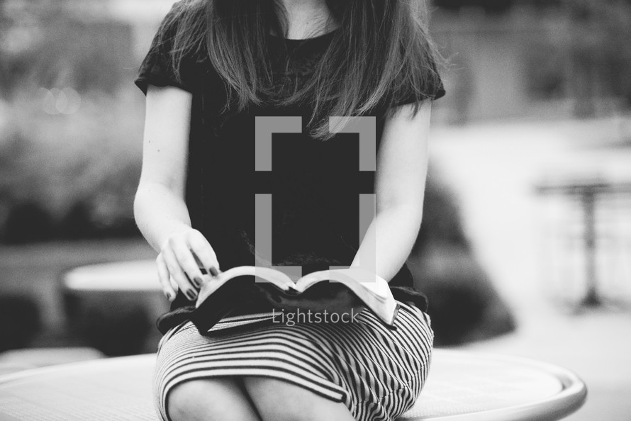 young woman sitting outdoors reading a Bible 