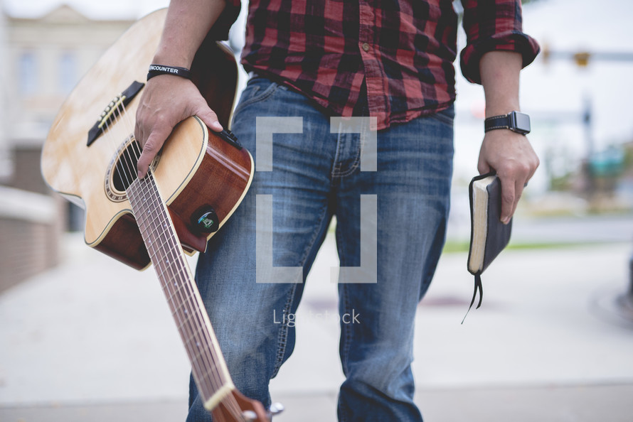man standing holding a guitar and Bible 