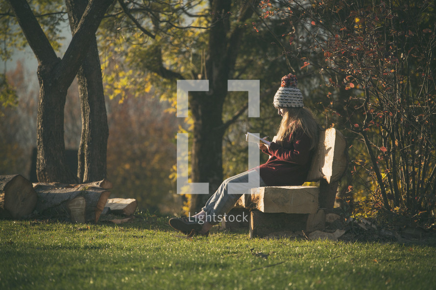 a teen girl sitting on a bench reading a bIble 