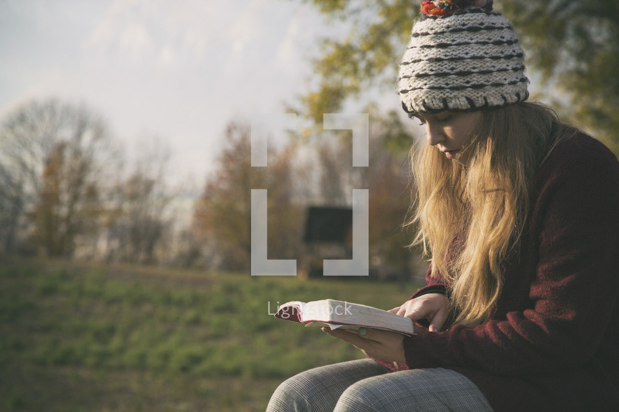 a teen girl reading a Bible on a bench outdoors