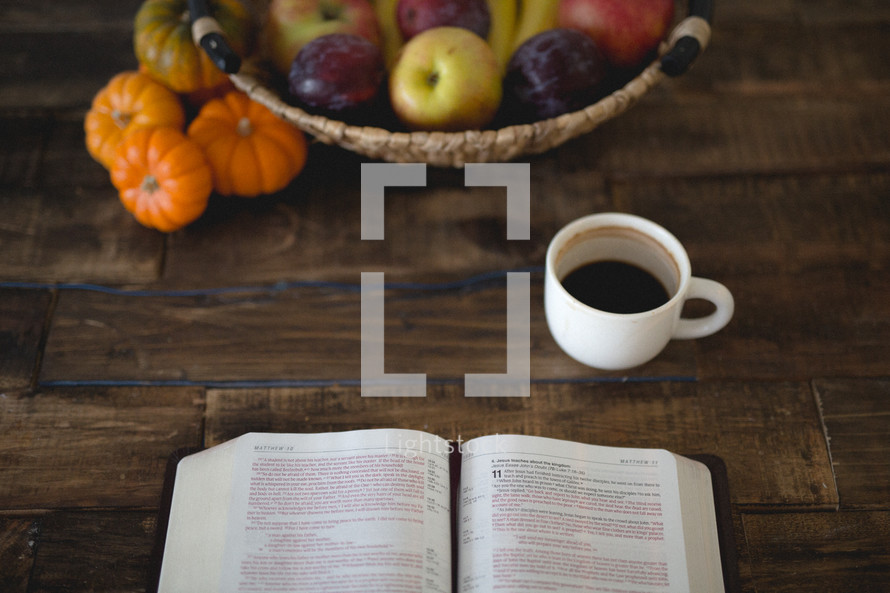 pumpkins, coffee mug, basket of plums and apples and open Bible