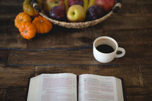 pumpkins, coffee mug, basket of plums and apples and open Bible