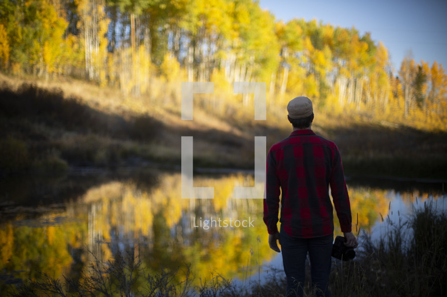 a man standing by a pond in fall 