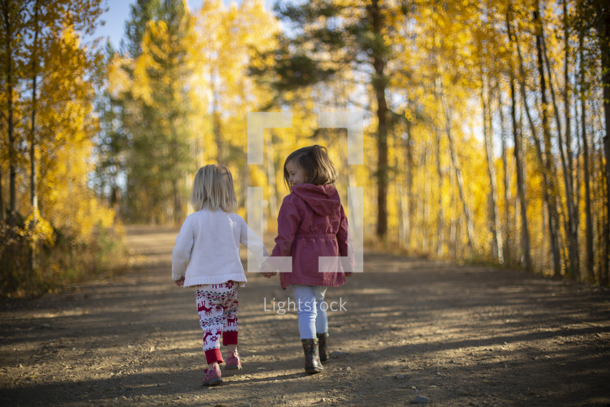 little girls walking outdoors on a dirt road in fall 
