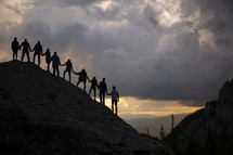 silhouette of friends holding hands on a mountainside 