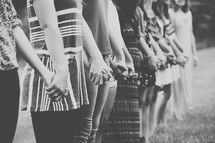 Line of women holding hands while standing in a field.