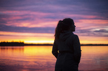 silhouette of a woman standing in front of a lake at sunset 