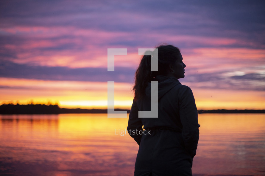 silhouette of a woman standing in front of a lake at sunset 