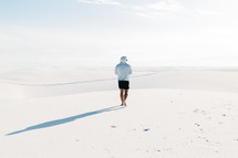 A single man wearing a hoodie walking through a sand filled desert barefoot