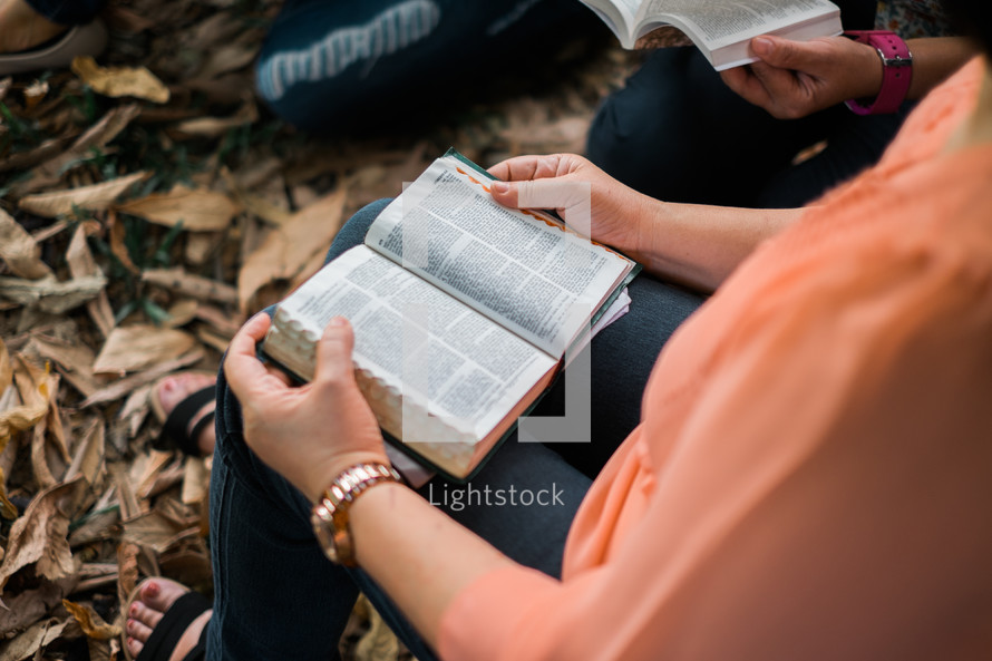 group reading a Bible over fall leaves on the ground 