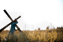 a man carrying a cross through a field 