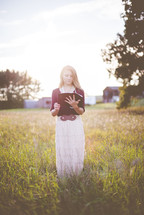 a woman standing in a field reading a Bible 