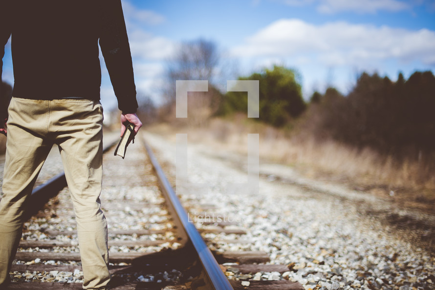 man standing in the middle of train tracks holding a Bible 