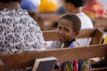 child sitting in a church pew looking at the camera 