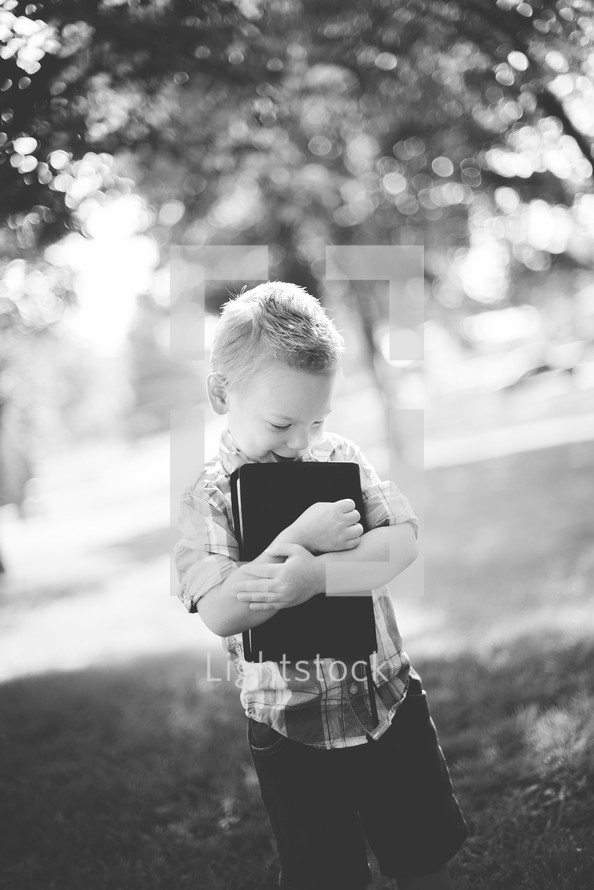 a toddler standing outdoors hugging a Bible 