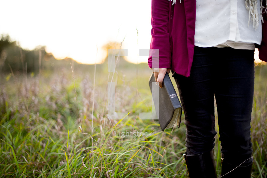 woman standing in a field holding a Bible 