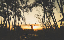 a person with raised hands standing outdoors at sunset 