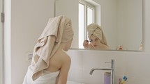 Teenage girl applying mascara in front of the bathroom mirror