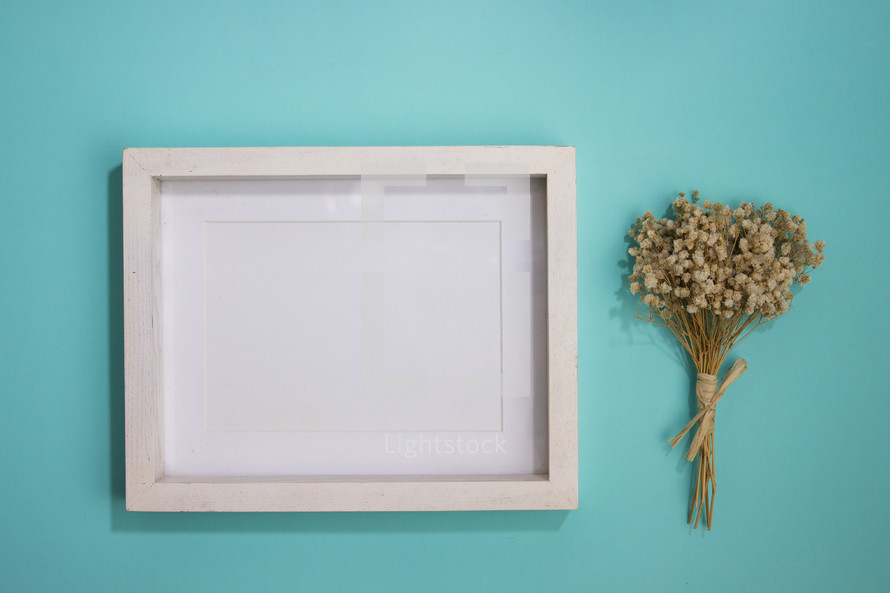 Blank white frame on turquoise background with bouquet