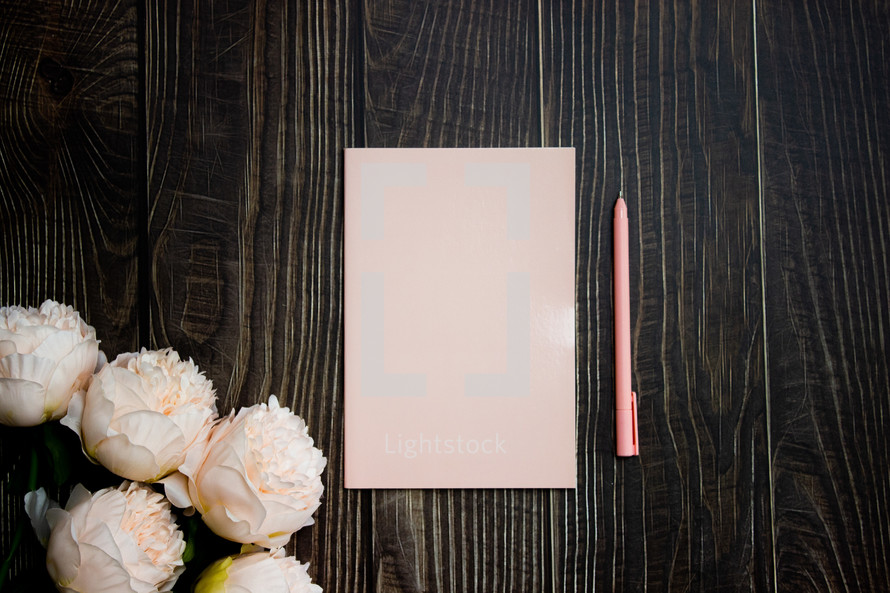 Pink notebook, pen, and flowers on wooden table