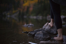 a woman standing on a lake shore in fall barefoot 