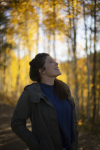 a young woman looking up at fall foliage 