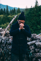 a man praying outdoors in front of firewood 