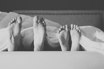 Parent's and child's feet sticking out from the blanket at the end of the bed.