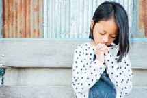 praying little girl in front of rusty sheet metal 