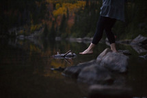 a woman standing on a fall lake shore dipping her toes in the water