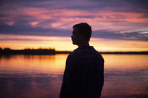 silhouette of a man standing in front of a lake at sunset 