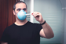 man with medical mask looking at a thermometer