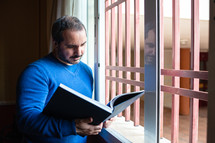 man reading a book by the window during quarantine