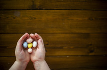 child with cupped hands holding candy Easter eggs 