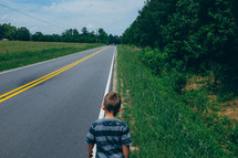 a boy child walking alone at the edge of a street 