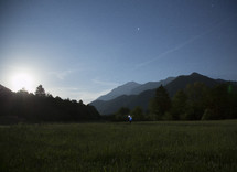 standing in a meadow surrounded by mountains with a flashlight 