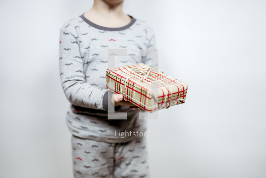 toddler boy in pajamas holding a Christmas present 