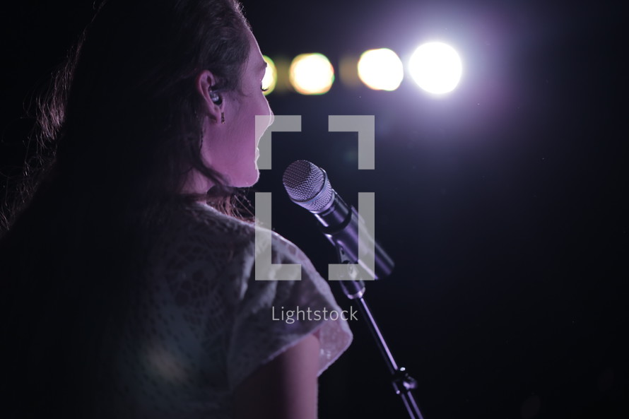Smiling woman standing at a microphone in front of lights.