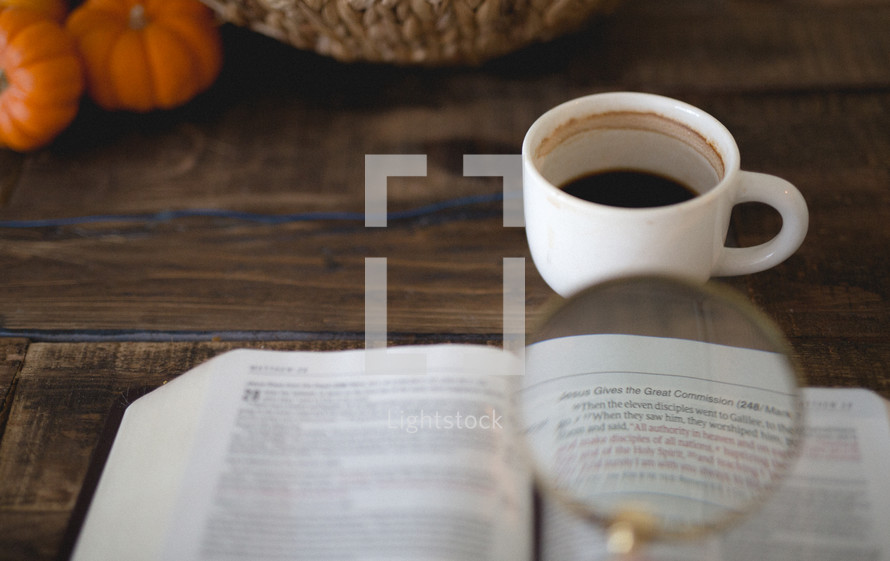 magnifying glass over the pages of a Bible, coffee mug, and pumpkins 