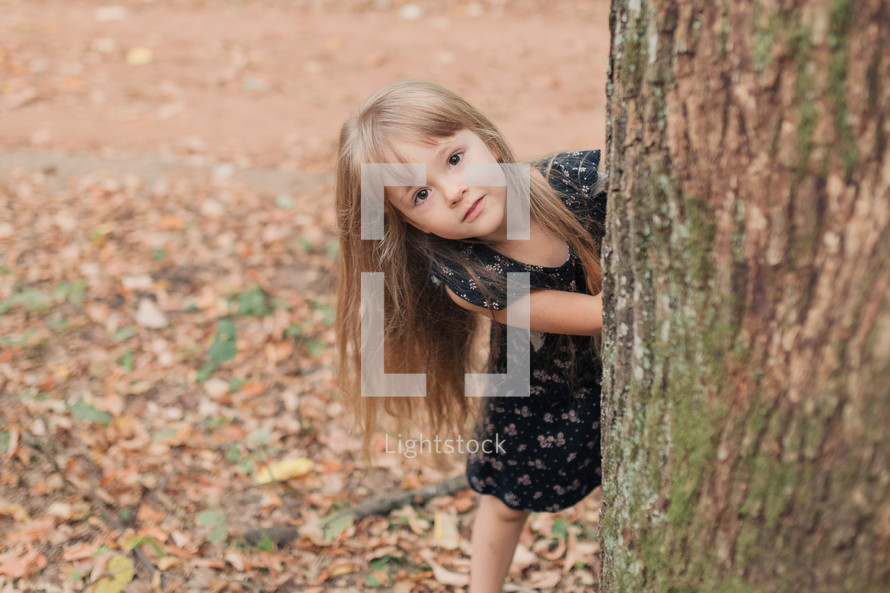 a girl peeking around a tree 