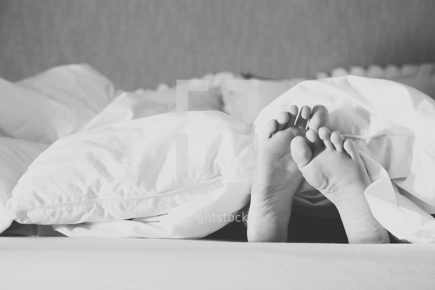 Child's feet sticking out from the blanket at the end of the bed.