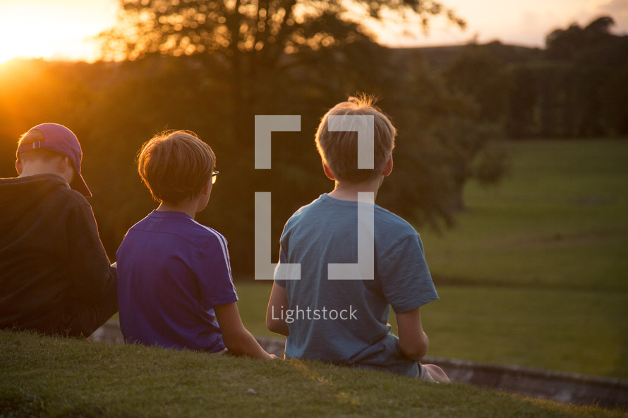 kids sitting on a wall looking out at a green pasture 
