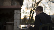 a man reading a Bible outdoors at a table 