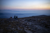 group sitting on a mountaintop watching the sunrise 